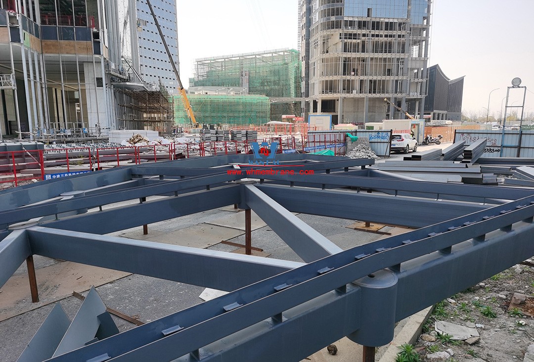 Recently, Shaoxing Huafa Financial Vitality City ETFE membrane structure commercial canopy ushered in new progress.  Shaoxing Huafa Financial Vitality City is located in Jinghu New District, Yuecheng District, Shaoxing City, 7.5km away from Shaoxing City Center, east to Xingzhong Road, west to Wenxian Road, south to Qunxian Road, north to Kwun Tong Road West. Huafa Financial Vitality City is the first commercial flagship brand of Guomai Huafa into Zhejiang, based on the history and future of Shaoxing, located in Jinghu high-end core, to create a construction surface of about 70,000 square meters of MALL BLOCK commercial street combination of urban creative consumption space. The vertical support system of the main steel structure of the canopy is a tree structure, the horizontal support system is a double-curved box lattice shell structure, and the steel columns and diagonal braces are all hoisted in a single hoisting mode. The roof lattice shell is assembled in blocks by automobile crane on the ground, and the crawler crane is hoisted in blocks. Finally, it is covered with ETFE film (soft glass). Make the whole commercial street more transparent and bright, dazzling.   The steel structure installation and splicing work is being carried out at the site. Due to the narrow space, the steel structure hoisting operation radius is large, and the on-site welding amount is large, and the recent attacks of high temperature and heavy rain have brought many tests to the project. According to the actual working conditions on the site, Marriott disassembled the steel structure hoisting section and calculated the hoisting equipment; And according to the actual situation of the project to organize relevant technical personnel to carry out targeted learning and understanding, multiple training. Establish BIM model to guide factory processing and on-site installation, adopt high-precision laser cutting, organize processing personnel and construction personnel to disclose information in special meetings, fully understand drawings and models, and provide a strong guarantee for project construction. Engineering quality is the control focus of each project, and this project is included in the company's key control projects. Throughout the construction process of the project, Marriott has always focused on this quality goal, increased human and material input, strengthened management, carried forward the company's key projects, and done a good job in the spirit of each project, implementing quality target management. In order to achieve the goal, Marriott has implemented the target value to each team according to the project, the responsibility to the person, and the site construction is meticulous. In order to ensure the smooth progress of the project, the construction staff of Marriott planned for the rainy day, inverted the schedule, thorough deployment, coordinated the allocation of resources from various parties, coordinated the allocation of personnel, materials and machines, communicated the operation technology and safety technology of the operation team in advance, and assembled, tested, accepted and obtained evidence of the steel structure mesh shell. During the construction process, in the face of hot and rainy summer weather, the engineering Department does a good job of heat prevention and flood control measures to ensure the safety of construction personnel, and fully promote the construction progress, all the construction personnel fight sunny days, grab rainy days, under the premise of ensuring safety and quality, and constantly promote the progress of steel structure assembly, creating conditions for the installation of membrane structure in the later period.   The smooth progress of the project laid a solid foundation for the completion of the 