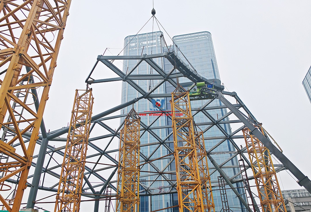 Recently, Shaoxing Huafa Financial Vitality City ETFE membrane structure commercial canopy ushered in new progress.  Shaoxing Huafa Financial Vitality City is located in Jinghu New District, Yuecheng District, Shaoxing City, 7.5km away from Shaoxing City Center, east to Xingzhong Road, west to Wenxian Road, south to Qunxian Road, north to Kwun Tong Road West. Huafa Financial Vitality City is the first commercial flagship brand of Guomai Huafa into Zhejiang, based on the history and future of Shaoxing, located in Jinghu high-end core, to create a construction surface of about 70,000 square meters of MALL BLOCK commercial street combination of urban creative consumption space. The vertical support system of the main steel structure of the canopy is a tree structure, the horizontal support system is a double-curved box lattice shell structure, and the steel columns and diagonal braces are all hoisted in a single hoisting mode. The roof lattice shell is assembled in blocks by automobile crane on the ground, and the crawler crane is hoisted in blocks. Finally, it is covered with ETFE film (soft glass). Make the whole commercial street more transparent and bright, dazzling.   The steel structure installation and splicing work is being carried out at the site. Due to the narrow space, the steel structure hoisting operation radius is large, and the on-site welding amount is large, and the recent attacks of high temperature and heavy rain have brought many tests to the project. According to the actual working conditions on the site, Marriott disassembled the steel structure hoisting section and calculated the hoisting equipment; And according to the actual situation of the project to organize relevant technical personnel to carry out targeted learning and understanding, multiple training. Establish BIM model to guide factory processing and on-site installation, adopt high-precision laser cutting, organize processing personnel and construction personnel to disclose information in special meetings, fully understand drawings and models, and provide a strong guarantee for project construction. Engineering quality is the control focus of each project, and this project is included in the company's key control projects. Throughout the construction process of the project, Marriott has always focused on this quality goal, increased human and material input, strengthened management, carried forward the company's key projects, and done a good job in the spirit of each project, implementing quality target management. In order to achieve the goal, Marriott has implemented the target value to each team according to the project, the responsibility to the person, and the site construction is meticulous. In order to ensure the smooth progress of the project, the construction staff of Marriott planned for the rainy day, inverted the schedule, thorough deployment, coordinated the allocation of resources from various parties, coordinated the allocation of personnel, materials and machines, communicated the operation technology and safety technology of the operation team in advance, and assembled, tested, accepted and obtained evidence of the steel structure mesh shell. During the construction process, in the face of hot and rainy summer weather, the engineering Department does a good job of heat prevention and flood control measures to ensure the safety of construction personnel, and fully promote the construction progress, all the construction personnel fight sunny days, grab rainy days, under the premise of ensuring safety and quality, and constantly promote the progress of steel structure assembly, creating conditions for the installation of membrane structure in the later period.   The smooth progress of the project laid a solid foundation for the completion of the 