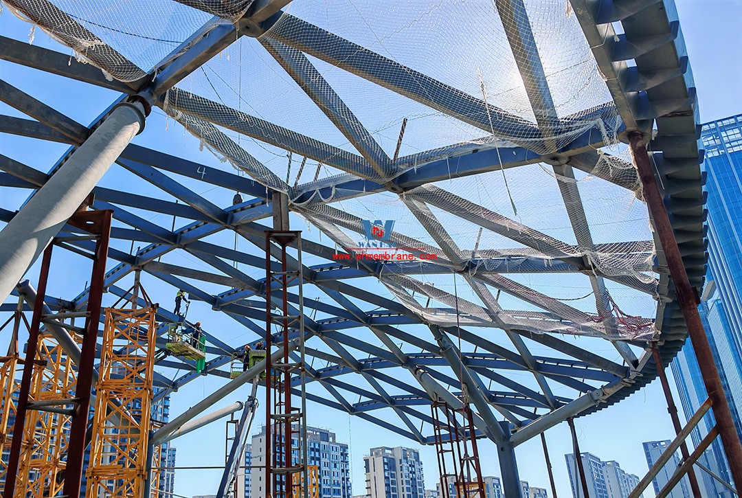 Recently, Shaoxing Huafa Financial Vitality City ETFE membrane structure commercial canopy ushered in new progress.  Shaoxing Huafa Financial Vitality City is located in Jinghu New District, Yuecheng District, Shaoxing City, 7.5km away from Shaoxing City Center, east to Xingzhong Road, west to Wenxian Road, south to Qunxian Road, north to Kwun Tong Road West. Huafa Financial Vitality City is the first commercial flagship brand of Guomai Huafa into Zhejiang, based on the history and future of Shaoxing, located in Jinghu high-end core, to create a construction surface of about 70,000 square meters of MALL BLOCK commercial street combination of urban creative consumption space. The vertical support system of the main steel structure of the canopy is a tree structure, the horizontal support system is a double-curved box lattice shell structure, and the steel columns and diagonal braces are all hoisted in a single hoisting mode. The roof lattice shell is assembled in blocks by automobile crane on the ground, and the crawler crane is hoisted in blocks. Finally, it is covered with ETFE film (soft glass). Make the whole commercial street more transparent and bright, dazzling.   The steel structure installation and splicing work is being carried out at the site. Due to the narrow space, the steel structure hoisting operation radius is large, and the on-site welding amount is large, and the recent attacks of high temperature and heavy rain have brought many tests to the project. According to the actual working conditions on the site, Marriott disassembled the steel structure hoisting section and calculated the hoisting equipment; And according to the actual situation of the project to organize relevant technical personnel to carry out targeted learning and understanding, multiple training. Establish BIM model to guide factory processing and on-site installation, adopt high-precision laser cutting, organize processing personnel and construction personnel to disclose information in special meetings, fully understand drawings and models, and provide a strong guarantee for project construction. Engineering quality is the control focus of each project, and this project is included in the company's key control projects. Throughout the construction process of the project, Marriott has always focused on this quality goal, increased human and material input, strengthened management, carried forward the company's key projects, and done a good job in the spirit of each project, implementing quality target management. In order to achieve the goal, Marriott has implemented the target value to each team according to the project, the responsibility to the person, and the site construction is meticulous. In order to ensure the smooth progress of the project, the construction staff of Marriott planned for the rainy day, inverted the schedule, thorough deployment, coordinated the allocation of resources from various parties, coordinated the allocation of personnel, materials and machines, communicated the operation technology and safety technology of the operation team in advance, and assembled, tested, accepted and obtained evidence of the steel structure mesh shell. During the construction process, in the face of hot and rainy summer weather, the engineering Department does a good job of heat prevention and flood control measures to ensure the safety of construction personnel, and fully promote the construction progress, all the construction personnel fight sunny days, grab rainy days, under the premise of ensuring safety and quality, and constantly promote the progress of steel structure assembly, creating conditions for the installation of membrane structure in the later period.   The smooth progress of the project laid a solid foundation for the completion of the 