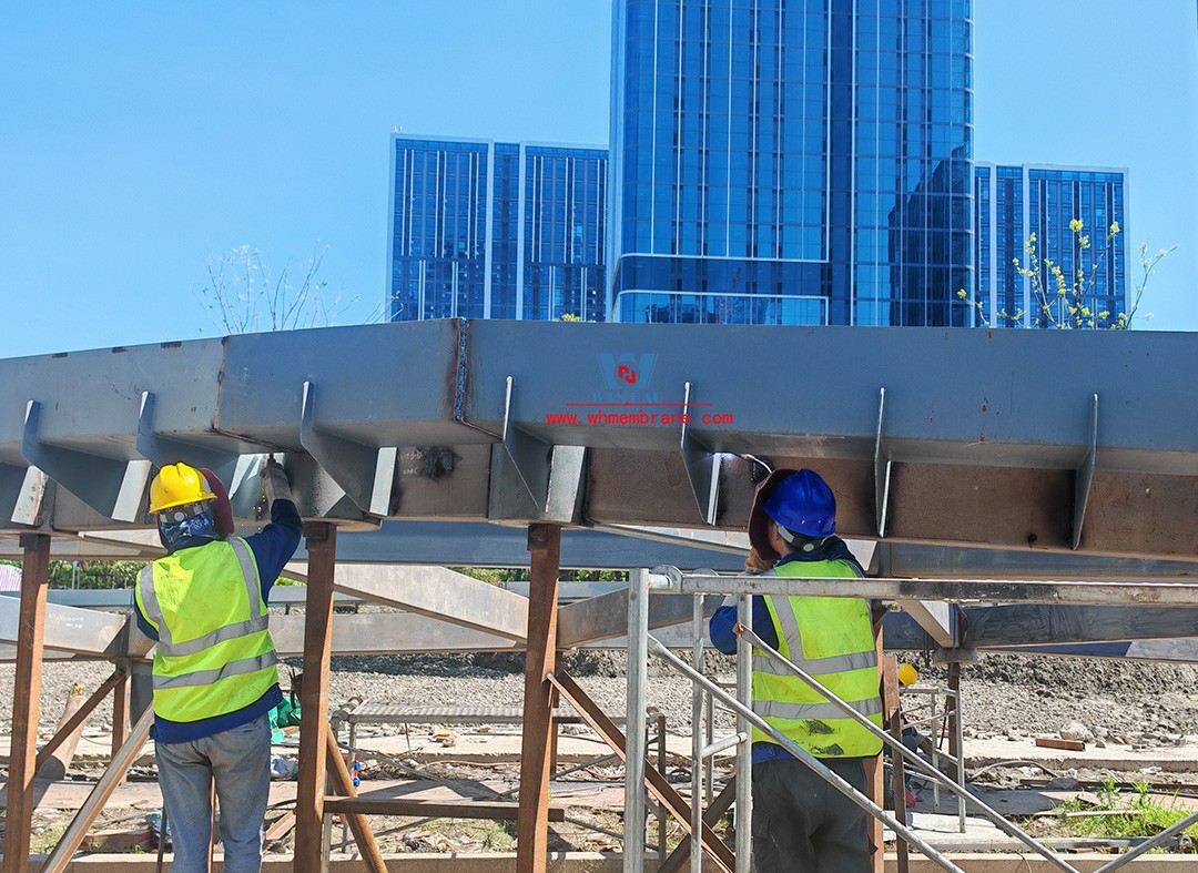Recently, Shaoxing Huafa Financial Vitality City ETFE membrane structure commercial canopy ushered in new progress.  Shaoxing Huafa Financial Vitality City is located in Jinghu New District, Yuecheng District, Shaoxing City, 7.5km away from Shaoxing City Center, east to Xingzhong Road, west to Wenxian Road, south to Qunxian Road, north to Kwun Tong Road West. Huafa Financial Vitality City is the first commercial flagship brand of Guomai Huafa into Zhejiang, based on the history and future of Shaoxing, located in Jinghu high-end core, to create a construction surface of about 70,000 square meters of MALL BLOCK commercial street combination of urban creative consumption space. The vertical support system of the main steel structure of the canopy is a tree structure, the horizontal support system is a double-curved box lattice shell structure, and the steel columns and diagonal braces are all hoisted in a single hoisting mode. The roof lattice shell is assembled in blocks by automobile crane on the ground, and the crawler crane is hoisted in blocks. Finally, it is covered with ETFE film (soft glass). Make the whole commercial street more transparent and bright, dazzling.   The steel structure installation and splicing work is being carried out at the site. Due to the narrow space, the steel structure hoisting operation radius is large, and the on-site welding amount is large, and the recent attacks of high temperature and heavy rain have brought many tests to the project. According to the actual working conditions on the site, Marriott disassembled the steel structure hoisting section and calculated the hoisting equipment; And according to the actual situation of the project to organize relevant technical personnel to carry out targeted learning and understanding, multiple training. Establish BIM model to guide factory processing and on-site installation, adopt high-precision laser cutting, organize processing personnel and construction personnel to disclose information in special meetings, fully understand drawings and models, and provide a strong guarantee for project construction. Engineering quality is the control focus of each project, and this project is included in the company's key control projects. Throughout the construction process of the project, Marriott has always focused on this quality goal, increased human and material input, strengthened management, carried forward the company's key projects, and done a good job in the spirit of each project, implementing quality target management. In order to achieve the goal, Marriott has implemented the target value to each team according to the project, the responsibility to the person, and the site construction is meticulous. In order to ensure the smooth progress of the project, the construction staff of Marriott planned for the rainy day, inverted the schedule, thorough deployment, coordinated the allocation of resources from various parties, coordinated the allocation of personnel, materials and machines, communicated the operation technology and safety technology of the operation team in advance, and assembled, tested, accepted and obtained evidence of the steel structure mesh shell. During the construction process, in the face of hot and rainy summer weather, the engineering Department does a good job of heat prevention and flood control measures to ensure the safety of construction personnel, and fully promote the construction progress, all the construction personnel fight sunny days, grab rainy days, under the premise of ensuring safety and quality, and constantly promote the progress of steel structure assembly, creating conditions for the installation of membrane structure in the later period.   The smooth progress of the project laid a solid foundation for the completion of the 