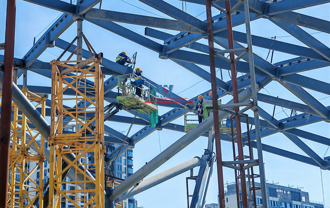 Recently, Shaoxing Huafa Financial Vitality City ETFE membrane structure commercial canopy ushered in new progress.  Shaoxing Huafa Financial Vitality City is located in Jinghu New District, Yuecheng District, Shaoxing City, 7.5km away from Shaoxing City Center, east to Xingzhong Road, west to Wenxian Road, south to Qunxian Road, north to Kwun Tong Road West. Huafa Financial Vitality City is the first commercial flagship brand of Guomai Huafa into Zhejiang, based on the history and future of Shaoxing, located in Jinghu high-end core, to create a construction surface of about 70,000 square meters of MALL BLOCK commercial street combination of urban creative consumption space. The vertical support system of the main steel structure of the canopy is a tree structure, the horizontal support system is a double-curved box lattice shell structure, and the steel columns and diagonal braces are all hoisted in a single hoisting mode. The roof lattice shell is assembled in blocks by automobile crane on the ground, and the crawler crane is hoisted in blocks. Finally, it is covered with ETFE film (soft glass). Make the whole commercial street more transparent and bright, dazzling.   The steel structure installation and splicing work is being carried out at the site. Due to the narrow space, the steel structure hoisting operation radius is large, and the on-site welding amount is large, and the recent attacks of high temperature and heavy rain have brought many tests to the project. According to the actual working conditions on the site, Marriott disassembled the steel structure hoisting section and calculated the hoisting equipment; And according to the actual situation of the project to organize relevant technical personnel to carry out targeted learning and understanding, multiple training. Establish BIM model to guide factory processing and on-site installation, adopt high-precision laser cutting, organize processing personnel and construction personnel to disclose information in special meetings, fully understand drawings and models, and provide a strong guarantee for project construction. Engineering quality is the control focus of each project, and this project is included in the company's key control projects. Throughout the construction process of the project, Marriott has always focused on this quality goal, increased human and material input, strengthened management, carried forward the company's key projects, and done a good job in the spirit of each project, implementing quality target management. In order to achieve the goal, Marriott has implemented the target value to each team according to the project, the responsibility to the person, and the site construction is meticulous. In order to ensure the smooth progress of the project, the construction staff of Marriott planned for the rainy day, inverted the schedule, thorough deployment, coordinated the allocation of resources from various parties, coordinated the allocation of personnel, materials and machines, communicated the operation technology and safety technology of the operation team in advance, and assembled, tested, accepted and obtained evidence of the steel structure mesh shell. During the construction process, in the face of hot and rainy summer weather, the engineering Department does a good job of heat prevention and flood control measures to ensure the safety of construction personnel, and fully promote the construction progress, all the construction personnel fight sunny days, grab rainy days, under the premise of ensuring safety and quality, and constantly promote the progress of steel structure assembly, creating conditions for the installation of membrane structure in the later period.   The smooth progress of the project laid a solid foundation for the completion of the 